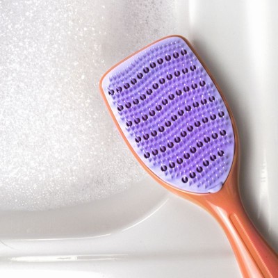 Brosse démêlante Agamy corail et picots violets en cours de nettoyage dans un lavabo – tête lavable et hygiénique
