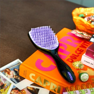Brosse démêlante Agamy noire avec picots violets posée sur livre orange “Capri Dolce Vita”,anti-casse et tous types de cheveux