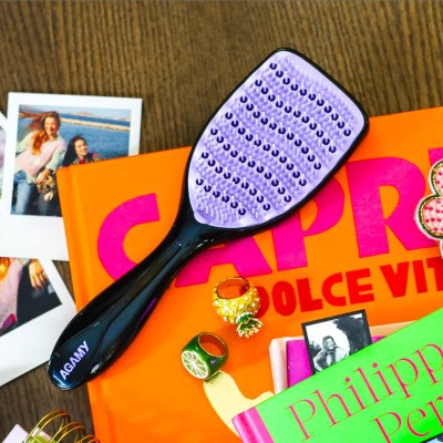 Brosse démêlante Agamy noire avec picots violets posée sur livre orange , brosse anti-casse et tous types de cheveux