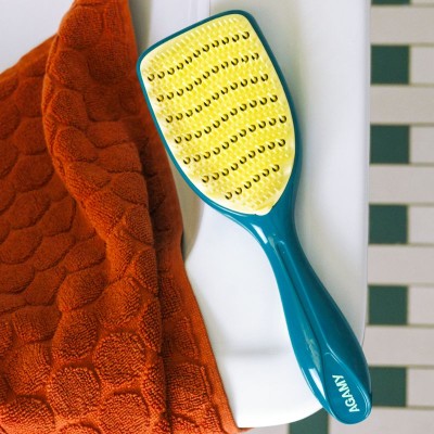 Grande brosse Agamy bleu canard et picots jaunes posée au bord de la baignoire avec serviette rouge à côté