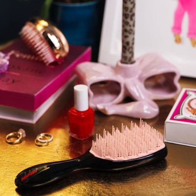 Brosse démêlante AGAMY petit modèle noire, avec logo rouge et picots crème, posée sur une coiffeuse dorée avec accessoires