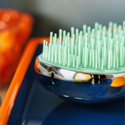 Brosse compacte AGAMY bleu marine avec picots verts et contour argenté, posée sur un plateau bleu et orange
