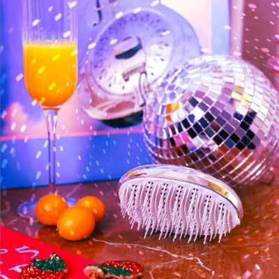 Brosse compacte AGAMY argentée posée sur une table en marbre, entourée de mandarines, boule disco et boisson festive