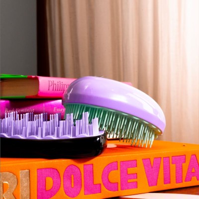 Brosse compacte AGAMY violette, design ergonomique pour démêlage, photo lifestyle avec livres colorés et déco tendance