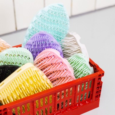 Têtes de brosses AGAMY multicolores rangées dans une caisse rouge, ambiance salle de bain avec carrelage blanc en arrière-plan.